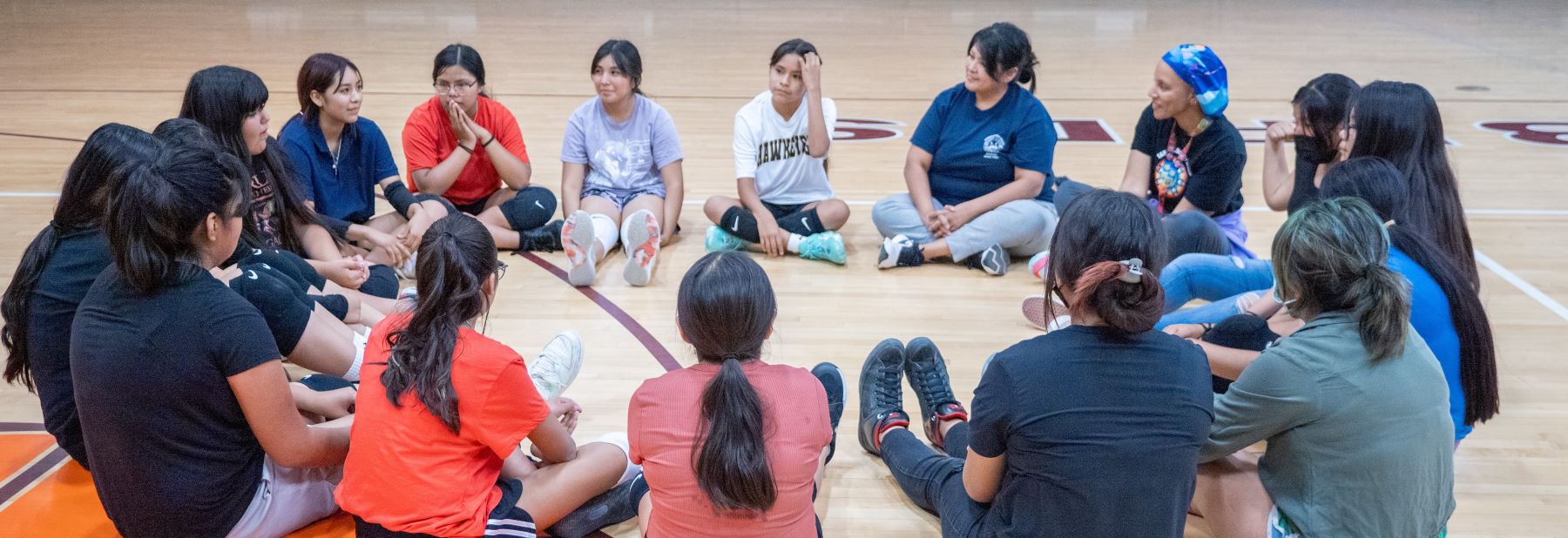 Students and teachers seated in a circle on the floor, engaged in conversation.