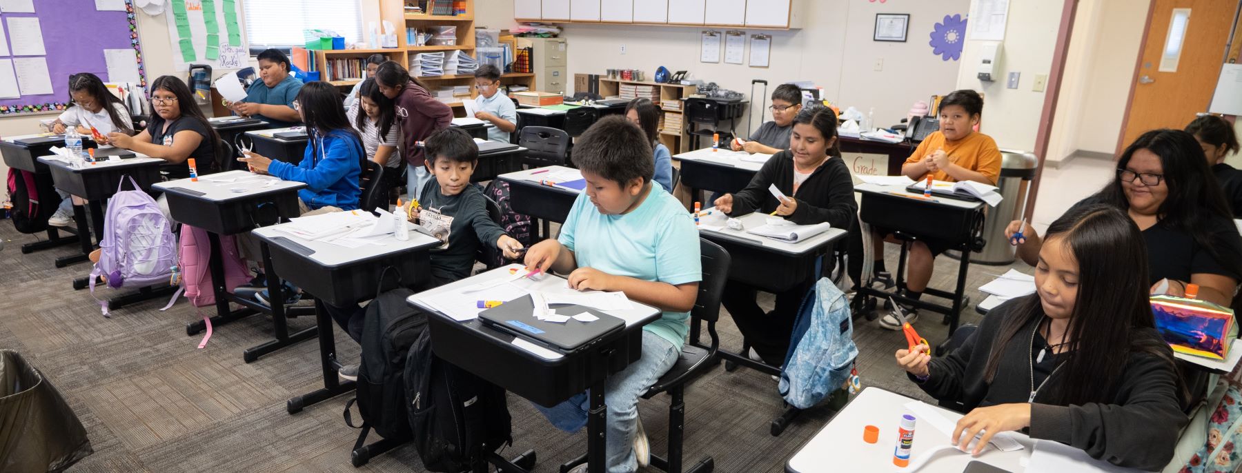 Classroom full of students sitting at their desks involved in various school activities.